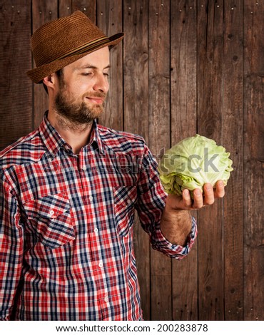 Happy smiling caucasian forty years old farmer or gardener in a hat holding cabbage in hand on rustic vintage planked wood background - agriculture. Food production - vegetables.