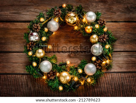Green christmas wreath decorated with gold balls, lights and pinecones on an old vintage planked wood background - rustic style