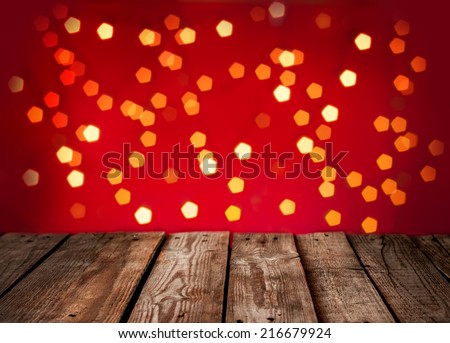 Christmas background - old vintage planked wood table in perspective on red backdrop with lights. Template with text space.