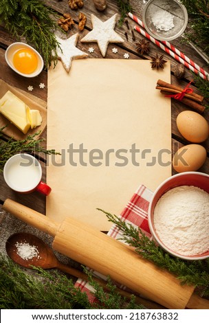 Christmas - baking cake background. Old sheet of paper with dough ingredients and decorations around on vintage planked wood table from above. Rural kitchen layout with free text space.