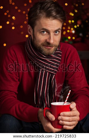 Christmas - happy smiling forty years old caucasian man holding hot drink or cocoa cup on dark red background with lights.