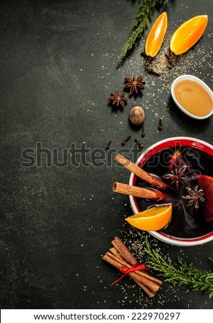 Hot mulled wine with orange slices, anise and cinnamon sticks on black chalkboard from above. Christmas or winter warming drink with recipe ingredients around. Layout with free text space.