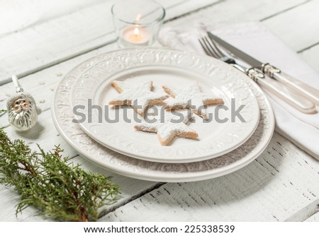 Christmas table setting - elegant white plate with cookies, natural pine tree branch and candle on vintage planked wood. Rustic or vintage style.