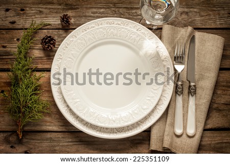 Vintage or rustic christmas table setting from above. Elegant empty white plate, cutlery on linen napkin and natural pine tree branch on rustic planked wood - country style.