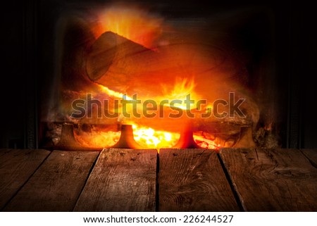 Fireplace and old vintage planked wood table in perspective. Burning firewood and flames as background.