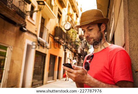 Forty years old caucasian tourist man looking at mobile phone outdoor near old city buildings - summer holiday