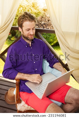 Happy smiling forty years old caucasian man looking at laptop computer on garden terrace during sunny summer day. Modern lifestyle - countryside weekend or freelance job concept.