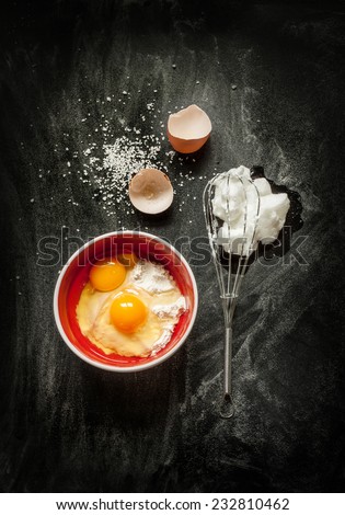 Baking cake ingredients - bowl, flour, eggs, egg whites foam, eggbeater and eggshells on black chalkboard from above. Cooking course poster concept - layout with free text space.