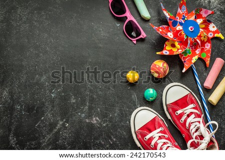 Toys and red sneakers on black chalkboard from above. Childhood - holiday or summer fun concept. Background layout with free text space.