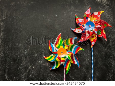 Colorful toy windmills on black chalkboard from above. Background layout with free text space.