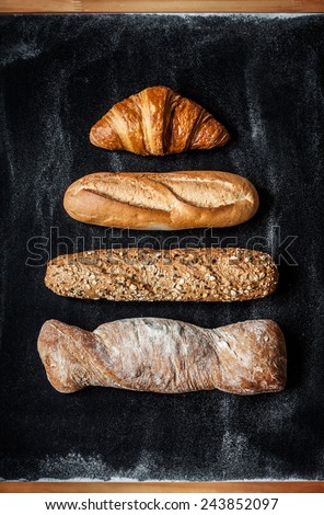 Different kinds of bread rolls on black chalkboard from above. Kitchen or bakery poster design.