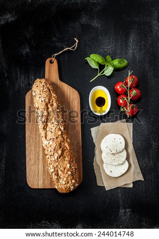 Sandwich recipe - bread roll, mozzarella cheese, cherry tomatoes and basil. Ingredients on black chalkboard from above. Poster layout with free text space.