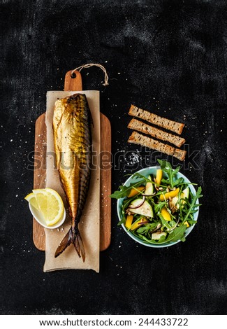 Smoked mackerel, fresh salad, croutons and lemon slices on black chalkboard background. Pub or bar table from above. Poster layout with free text space.