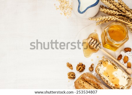 Rural or country breakfast - bread rolls, honey jar, milk, nuts, wheat and rolled oats on white wood from above. Background layout with free text space.