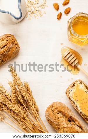 Rural or country breakfast - bread rolls, honey jar, milk, nuts, wheat and rolled oats on white wood from above. Background layout with free text space.