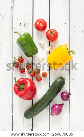 Mix of vegetables on white planked wood background - summer garden harvest. Red, yellow and green pepper, tomatoes, red onion, zucchini and garlic from above.