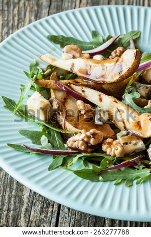 Salad - blue cheese, pear, arugula, walnuts, red onion and balsamic vinegar dressing on pastel blue plate close up.