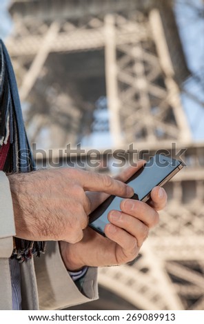 Man hands touching mobile phone screen (smartphone). Eiffel Tower as background. Tourist searching for information about Paris concept.
