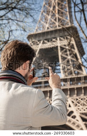 Caucasian tourist man takes a photo of Eiffel Tower in Paris with mobile phone (smartphone) - travelling.