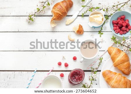 Romantic french or rural breakfast - cocoa, milk, croissants, jam, butter and raspberries on rustic white wooden table from above. Countryside weekend concept. Background layout with free text space.
