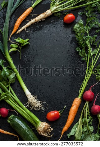 Young spring vegetables on black chalkboard from above. Background layout with free text space. Carrots, tomatoes, zucchini, leek, radish, celeriac, parsley and basil - fresh harvest from the garden.