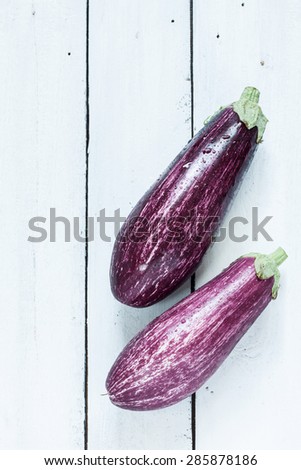 Purple eggplant (aubergine) on white planked wood table from above. Fresh harvest from the garden. Background layout with free text space.