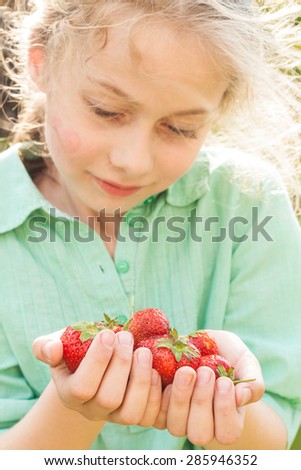 Blond caucasian seven years old child girl holding strawberries in hands. Spring - fresh harvest from the garden. Happy childhood concept.