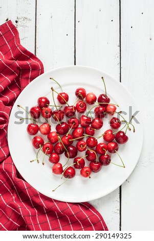 Fresh wet cherries on plate with red napkin. White planked wood table as background. Layout with free text space.