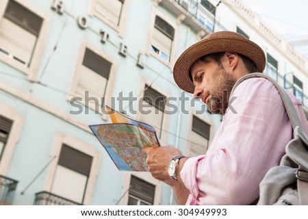 Forty years old caucasian tourist man with backpack looking at the city map outdoor. Vintage hotel as background. Summer holiday traveling.