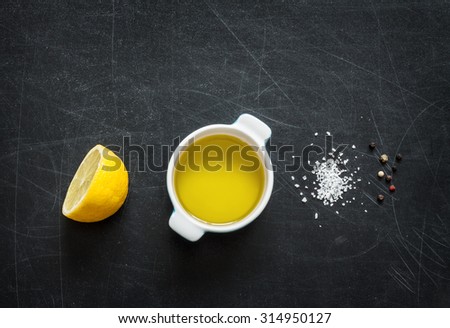 Lemon vinaigrette dressing ingredients on black chalkboard background from above. Lemon, olive oil, salt and pepper. Layout with free text space.