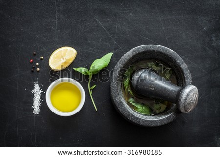 Basil vinaigrette dressing - recipe ingredients on black chalkboard background from above. Fresh basil leaves, lemon, olive oil, salt, pepper and mortar. Layout with free text space.