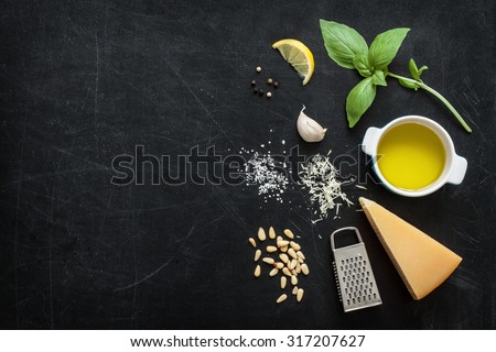 Green basil pesto - italian recipe ingredients on black chalkboard background from above. Parmesan cheese, basil leaves, pine nuts, olive oil, garlic, salt and pepper. Layout with free text space.
