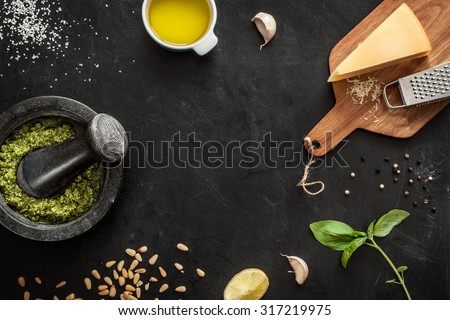 Green basil pesto - italian recipe ingredients on black chalkboard from above. Parmesan cheese, basil leaves, pine nuts, olive oil, garlic, salt, pepper and mortar. Layout with free text space.
