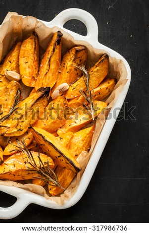 Roasted sweet potatoes in white ceramic dish close up from above. Black chalkboard as background.