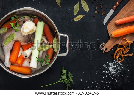 Preparing chicken stock (bouillon) with vegetables in a pot. Black chalkboard as background. Kitchen worktop scenery from above. Layout with free text space.