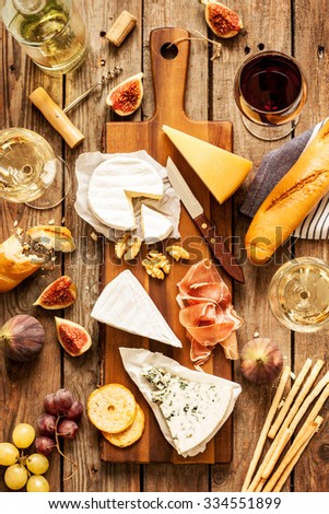 Different kinds of cheeses, wine, baguette, fruits and snacks on rustic wooden table from above. French tasting party or feast scenery.