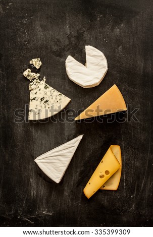 Different kinds of cheeses (camembert, brie, parmesan, blue cheese) captured from above (top view). Black chalkboard as background. Layout with free text space.