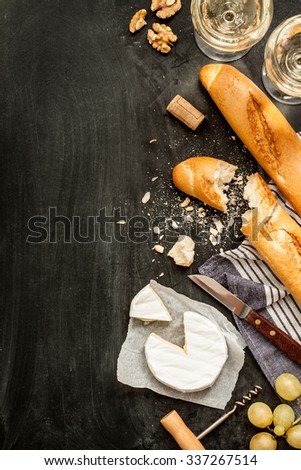 Camembert cheese, baguettes and two glasses of wine on black chalkboard background. Romantic french supper scenery captured from above (top view). Layout with free text space.