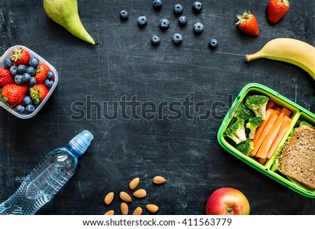 School lunch box with sandwich, vegetables, water, almonds and fruits on black chalkboard. Healthy eating habits concept - background layout with free text space. Flat lay composition (top view).