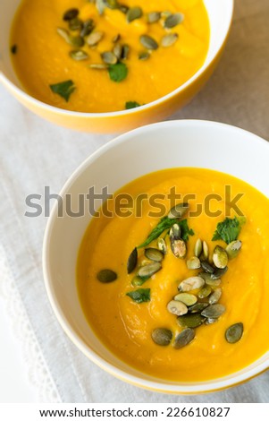 Two china bowls of homemade pumpkin soup with pumpkin seeds and herbs on laced table mat