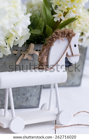 A white wooden horse with  row of three metal flower pots of yellow and white hyacinth on wood