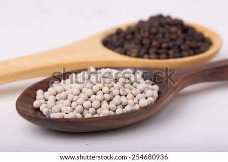 Black Pepper Corns and White Pepper Corns in wooden spoon on white background, Focus on White Pepper