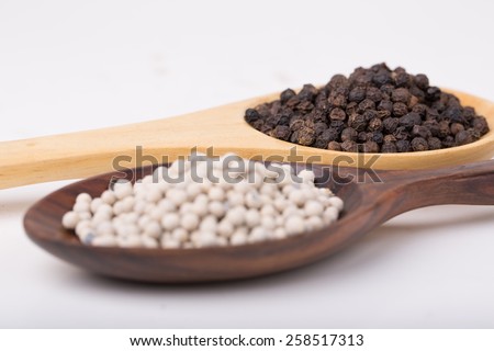 Black Pepper Corns and White Pepper Corns in wooden spoon on white background, Focus on Black Pepper
