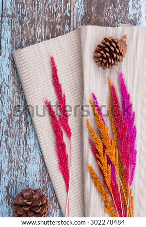 Dried grass flowers and light brown fabric with pinecone on blue wooden background