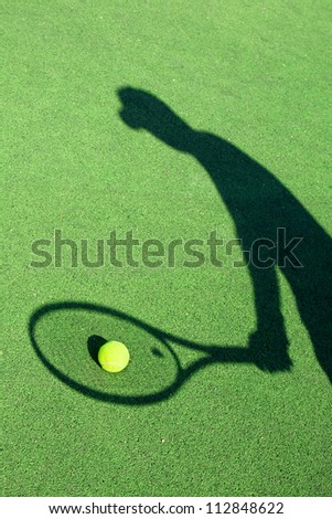 in action on a tennis court (conceptual image with a tennis ball lying on the court and the shadow of the player positioned in a way he seems to be playing it)
