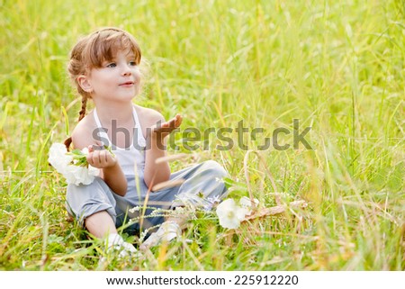 Little girl sitting in the grass and sends an air kiss