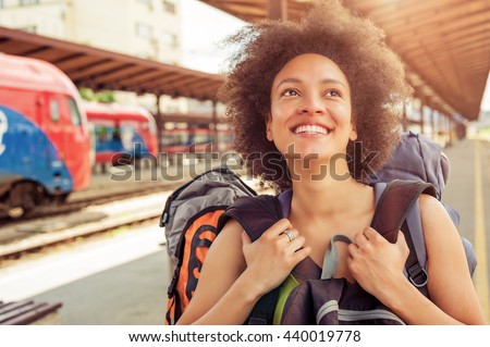 Closeup of beautiful tourist traveler standing with huge luggage at the railway station near the tracks