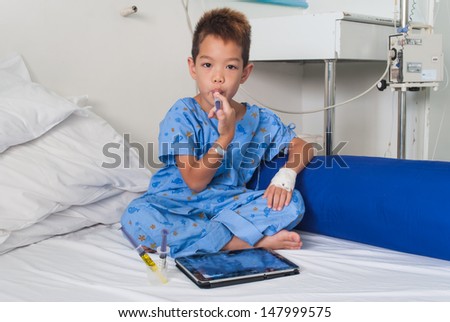 Asian patient boy with saline intravenous (iv) on hospital bed. Are using the tablet and eating medicines.