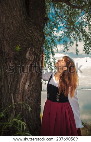 Beautiful romanian woman, dressed in popular costume, looking up tree