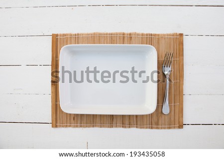 White squared plate with fork and a bamboo table cover on a white wooden table